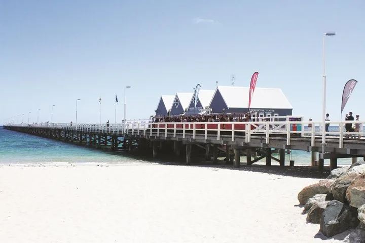 A wooden pier extending into the blue ocean from a sandy beach.