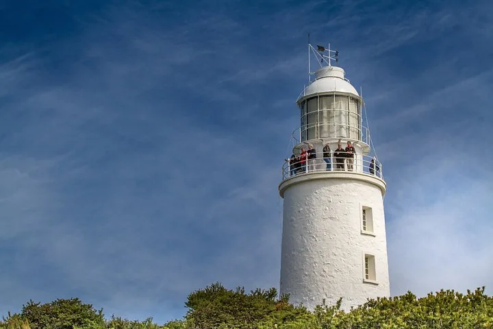 A group of people standing on the balcony of a white lighthouse.