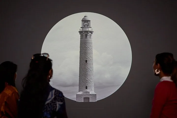 Two people looking at a circular projection of a lighthouse in an exhibit.