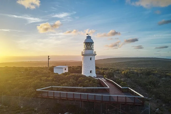 Cape Leeuwin Lighthouse viewed at sunset with a wooden viewing platform nearby.